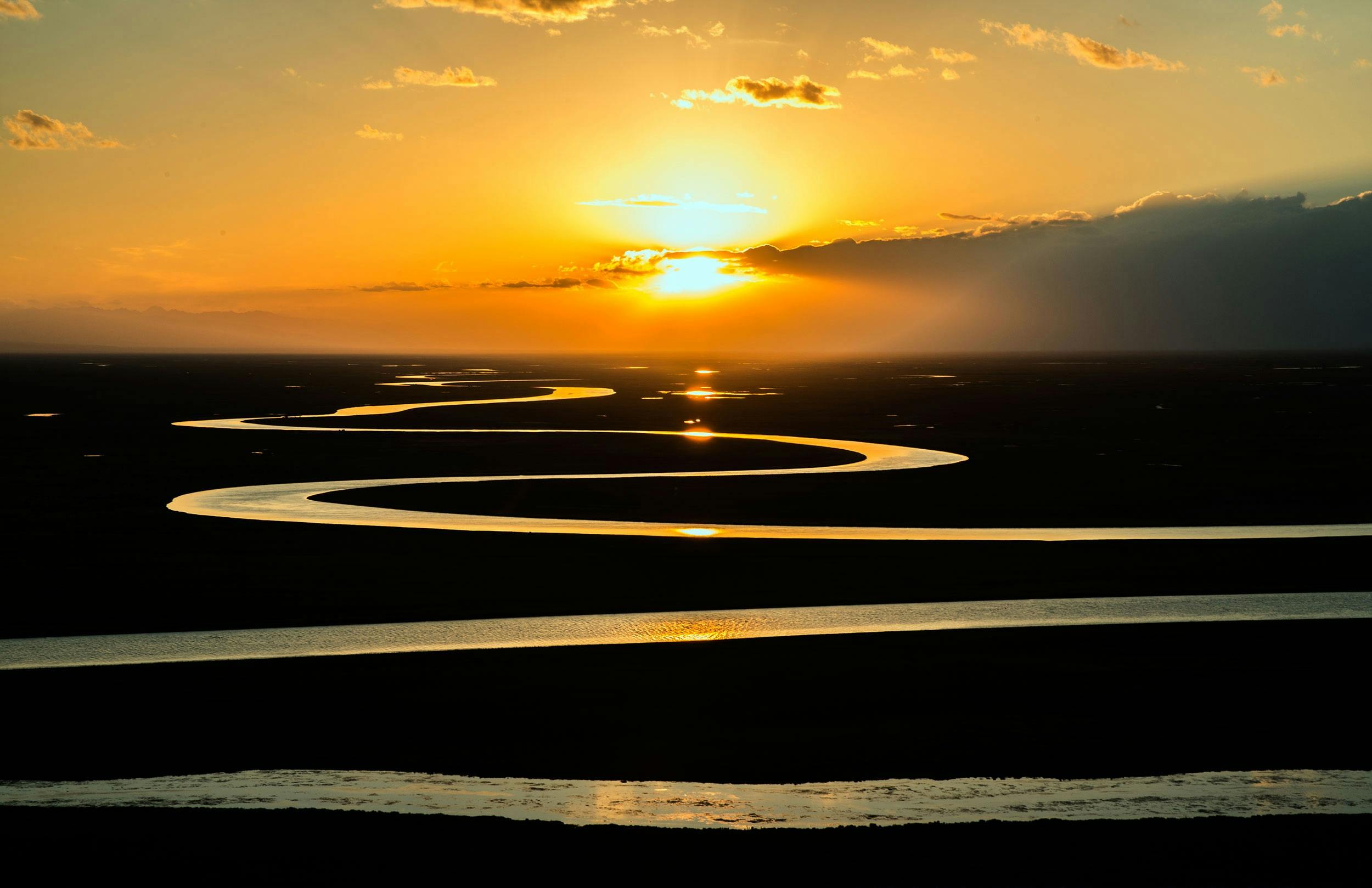 A meandering river flowing toward the setting sun on the horizon